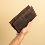 A hand displays the Leather Ladies Wallet Alice by Vintage Leather Sydney against a plain beige background, revealing a small circle tattoo on the wrist.