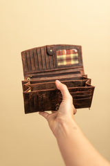 A hand holds an open Vintage Leather Sydney Leather Ladies Wallet Alice, showing multiple card slots, sections, and a small plaid-patterned ID window against a plain beige background.