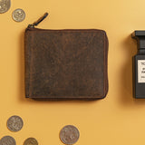 The Discover the Ultimate Mens Zipper Wallet – Urban by Vintage Leather Sydney, crafted from premium full grain leather, rests on a yellow surface with scattered coins and a black-capped Eau de Parfum bottle nearby.