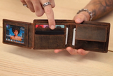 A person with rings and a bracelet points to the card slots inside an open Vintage Leather Sydney Mens Leather Trifold Wallet Braxton, which holds several cards. The RFID-protected wallet rests on a light wooden surface.