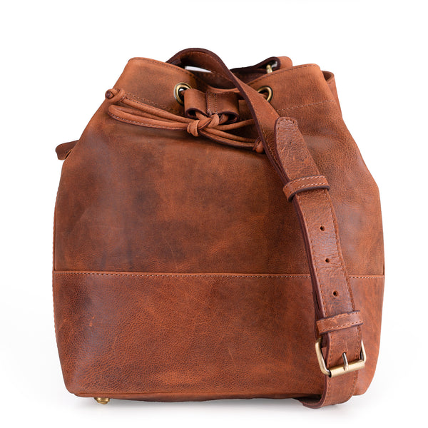 The Rosa Leather Crossbody Bag by Vintage Leather Sydney is a brown leather bucket bag with a shoulder strap, gold hardware, and a drawstring closure, featuring a spacious design against a white background.