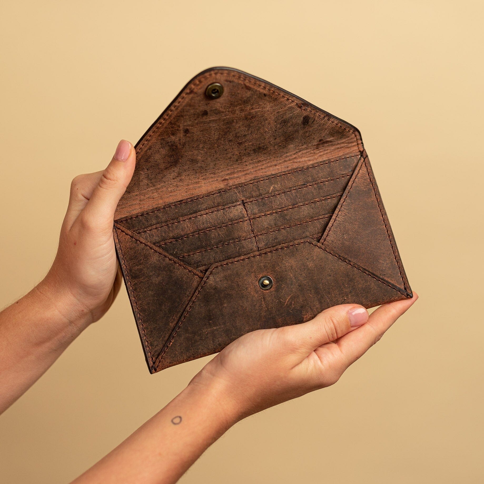 Two hands hold an open Vintage Leather Sydney Corda wallet for women, showcasing multiple card slots against a plain beige background.